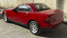 a red car with a black top is parked in front of a concrete wall