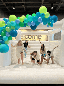 a group of women jumping on a bouncy house with balloons in front of a sign that says welcome