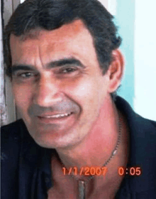 a man wearing a necklace and a black shirt is smiling for the camera with the date 1/1/2007