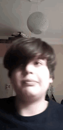 a young boy with short hair is making a funny face in a room with a ceiling fan hanging from the ceiling .