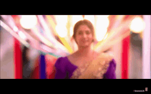 a blurred image of a woman in a purple top and gold saree