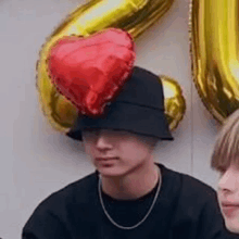 a man wearing a hat with a red heart shaped balloon on top of it .