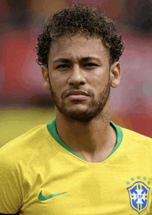 a man with curly hair and a beard is wearing a yellow shirt with a cbf logo on it