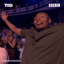 a man stands in front of a crowd with his arms in the air and a bbc logo in the background