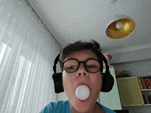 a boy wearing glasses and headphones blows a bubble