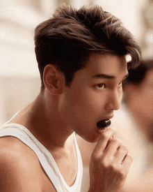 a young man in a white tank top is eating a cherry