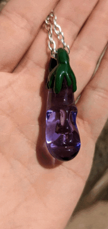 a person is holding a purple eggplant shaped pendant