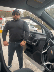 a man in a black sweater stands in front of a car door