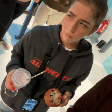 a woman wearing a black authentic hoodie holds a cookie and a milkshake