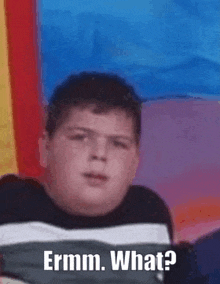 a fat boy is sitting in front of a colorful flag and making a funny face .