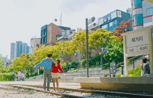 a man and a woman are standing on a train track in front of a sign that says ' chungguri ' on it