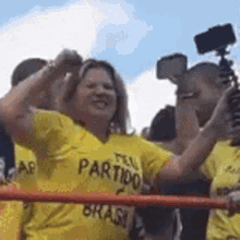 a woman in a yellow shirt with the word partido on it is standing in front of a crowd .