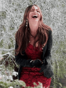 a woman in a red dress is laughing while standing in front of a tree