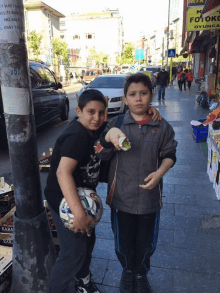 two boys standing on a sidewalk in front of a store called fotoko oyuncak