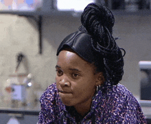 a woman with braids in her hair wearing a purple shirt and earrings