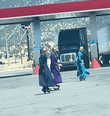 a group of women are walking down the street in front of a gas station .