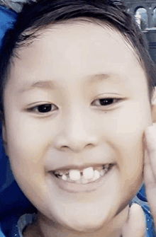 a young boy with missing teeth is smiling and holding his face .