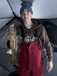 a young man holding a large fish wearing a shirt that says vert