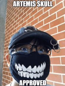 a person wearing a mask that says artemis skull approved is standing in front of a brick wall