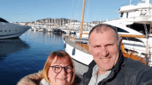 a man and a woman are posing for a picture in front of boats in a harbor