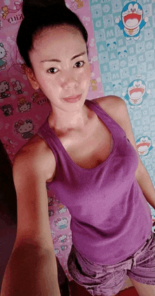 a woman in a purple tank top takes a selfie in front of a hello kitty wallpaper