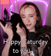 a woman with pink hair is holding a black cat and the words happy saturday to you