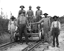 a black and white photo of a group of men standing on a train track