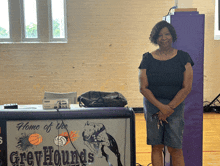 a woman stands in front of a sign for the greyhounds