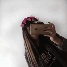 a woman is taking a selfie with her cell phone while wearing a hat with hearts on it .