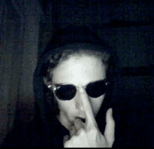 a man wearing sunglasses and a hood is covering his mouth with his hand .