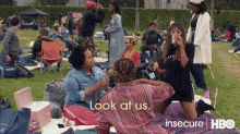 a group of women are sitting on a blanket in a park talking to each other and drinking wine .