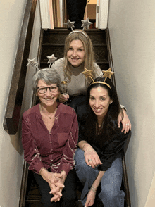 three women sitting on a set of stairs with one wearing a headband that says ' congratulations ' on it