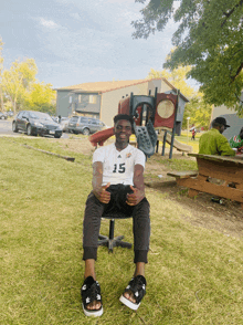 a man wearing a white shirt with the number 15 on it sits on a chair in front of a playground