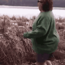 a woman in a green sweater is standing in a field of tall grass .