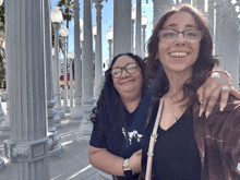 two women standing next to each other with one wearing glasses