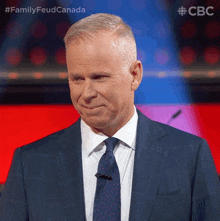 a man in a suit and tie stands in front of a microphone with the words family feud canada above him