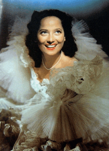 a woman wearing a white dress and a pearl necklace is smiling