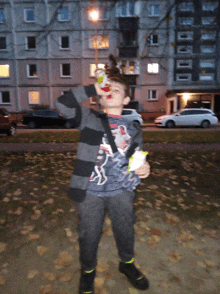 a young boy drinking from a can in front of a building with cars parked in front of it