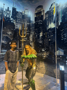 a man stands next to a statue of aquaman with a city in the background