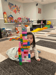 a little girl sits on the floor playing with a tower made of pink blocks with numbers 1 through 6 on them