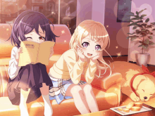 two anime girls sit on a couch reading a book while a dog sleeps on the couch