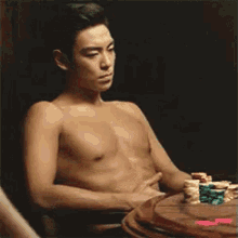 a shirtless man is sitting at a table with a pile of poker chips on it .