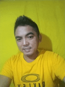 a man wearing a yellow oakley t-shirt takes a selfie