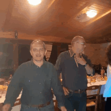 two men standing next to each other in a room with a wooden ceiling