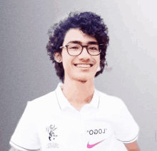 a young man wearing glasses and a white nike shirt smiles