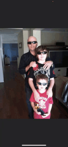 a man wearing sunglasses is standing next to two young boys one of whom is wearing a shirt that says jameson