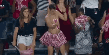 a man in a pink pom pom skirt is dancing in a crowd of people at a football game .