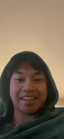 a man wearing a green hooded sweatshirt smiles for the camera