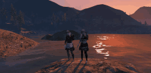 two people standing on a rock near a body of water with mountains in the background