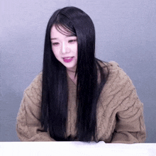 a girl with long black hair wearing a tan sweater